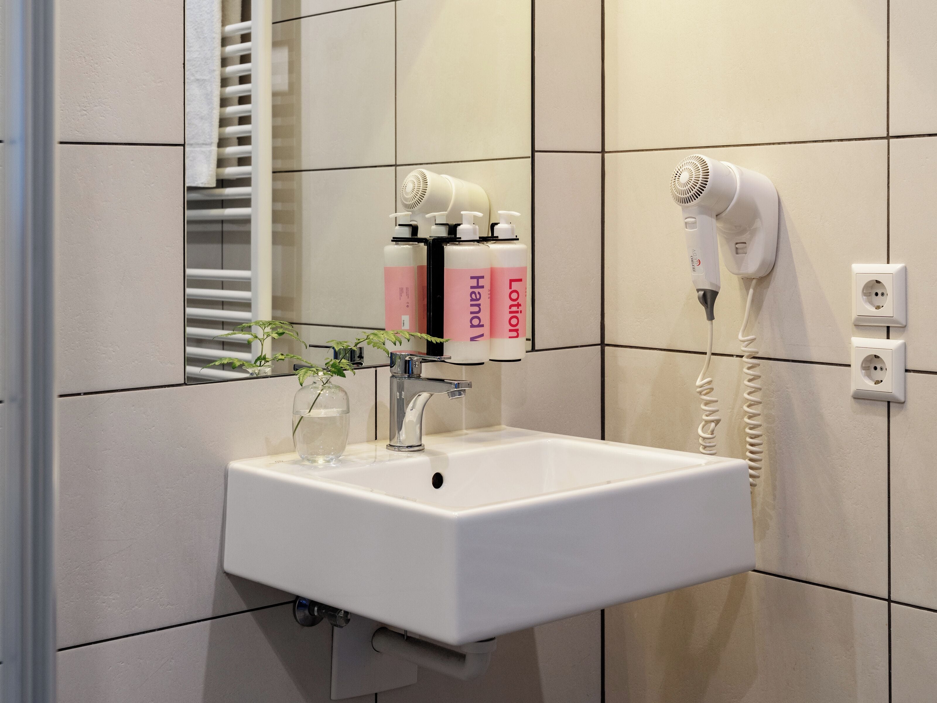 Ein Badezimmer mit einem weißen Waschbecken, einem Föhn und zwei Lotionflaschen.