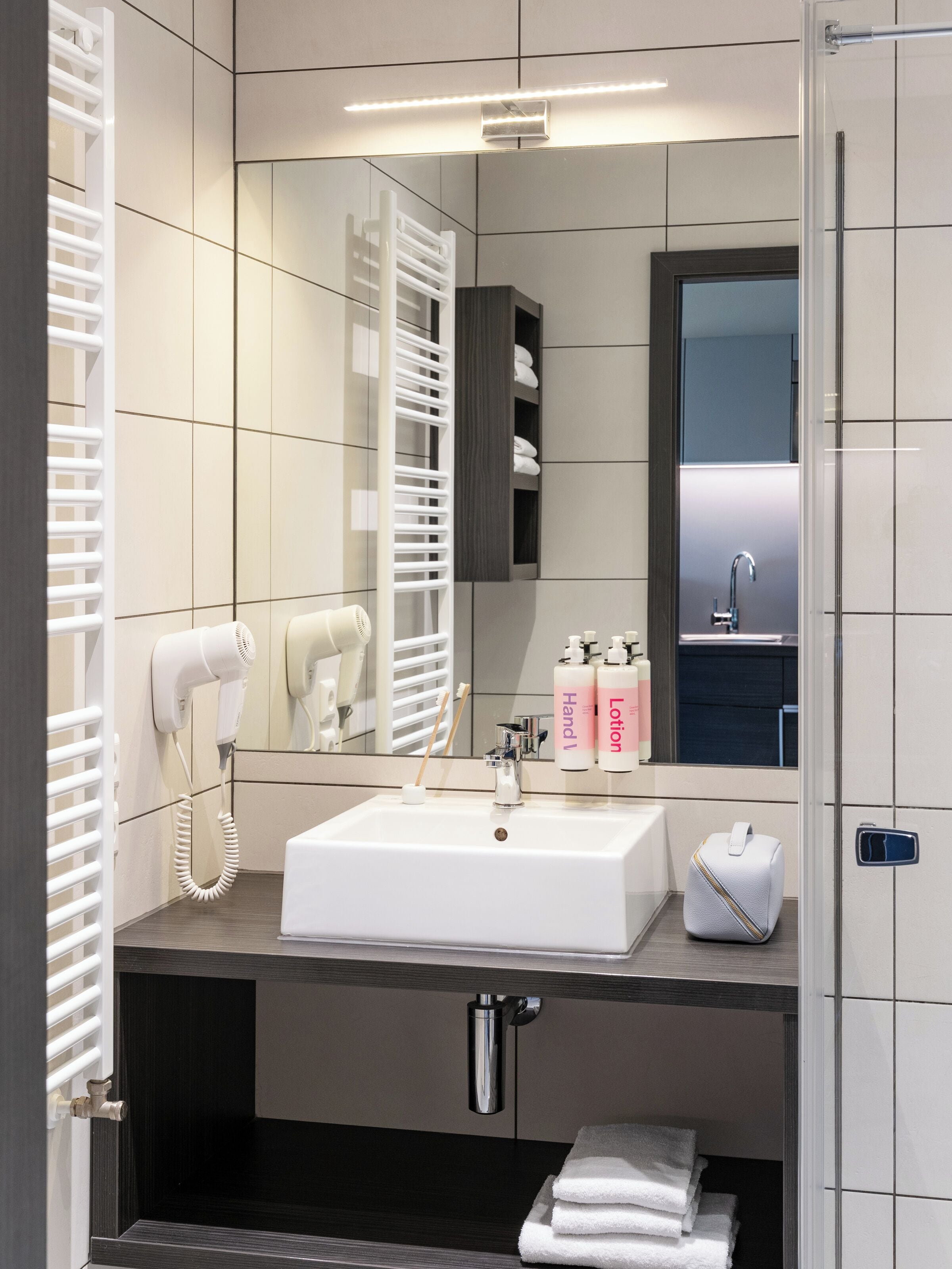 Ein modernes Badezimmer mit einem weißen Waschbecken, einem Spiegel, einem Handtuchhalter und einem Fön.