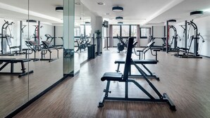 Une salle de sport moderne équipée de divers appareils d’exercice, dotée de grandes fenêtres et d’un plancher en bois.
