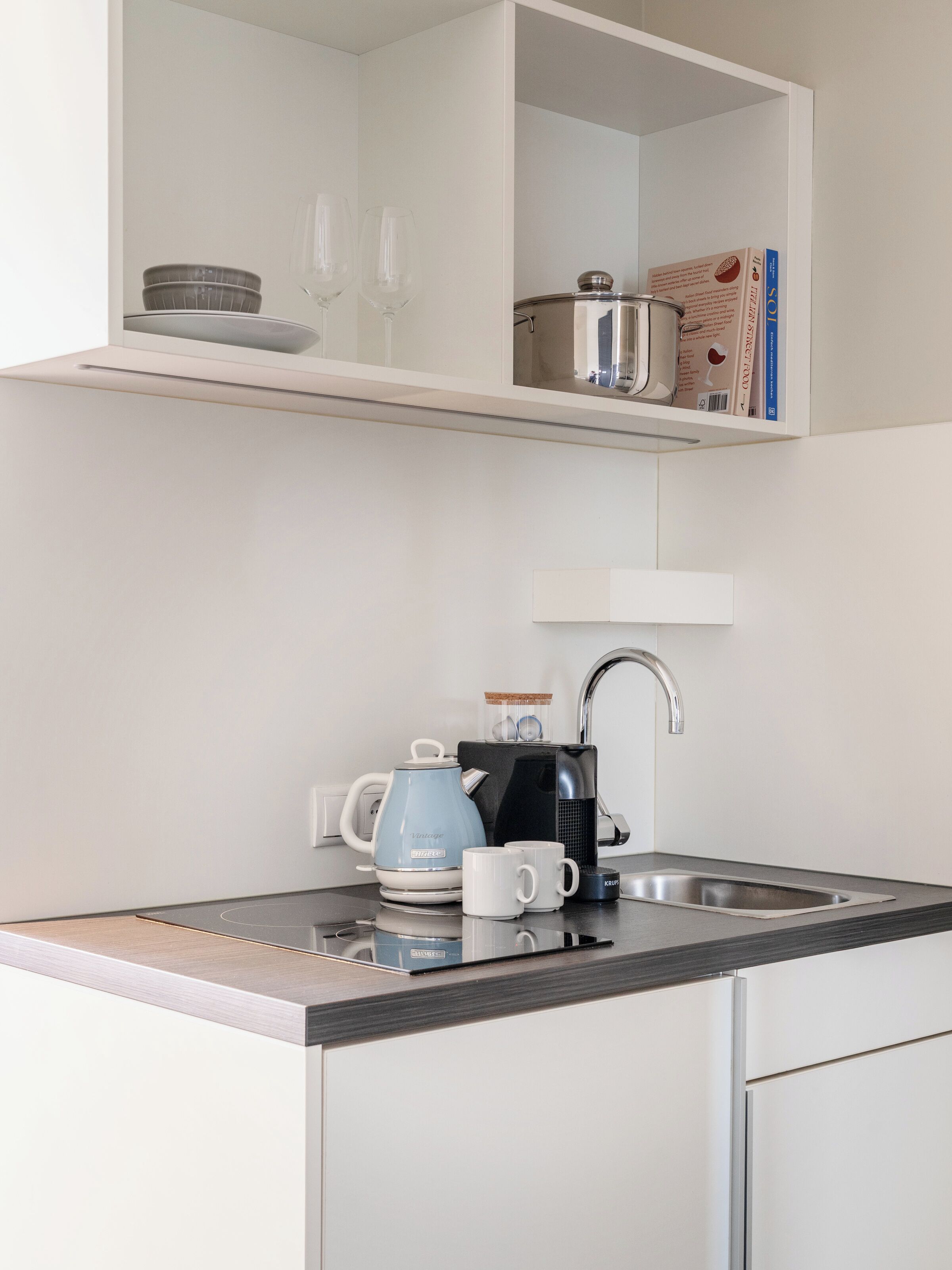 A modern kitchen with a built-in coffee maker, a kettle, and a sink.