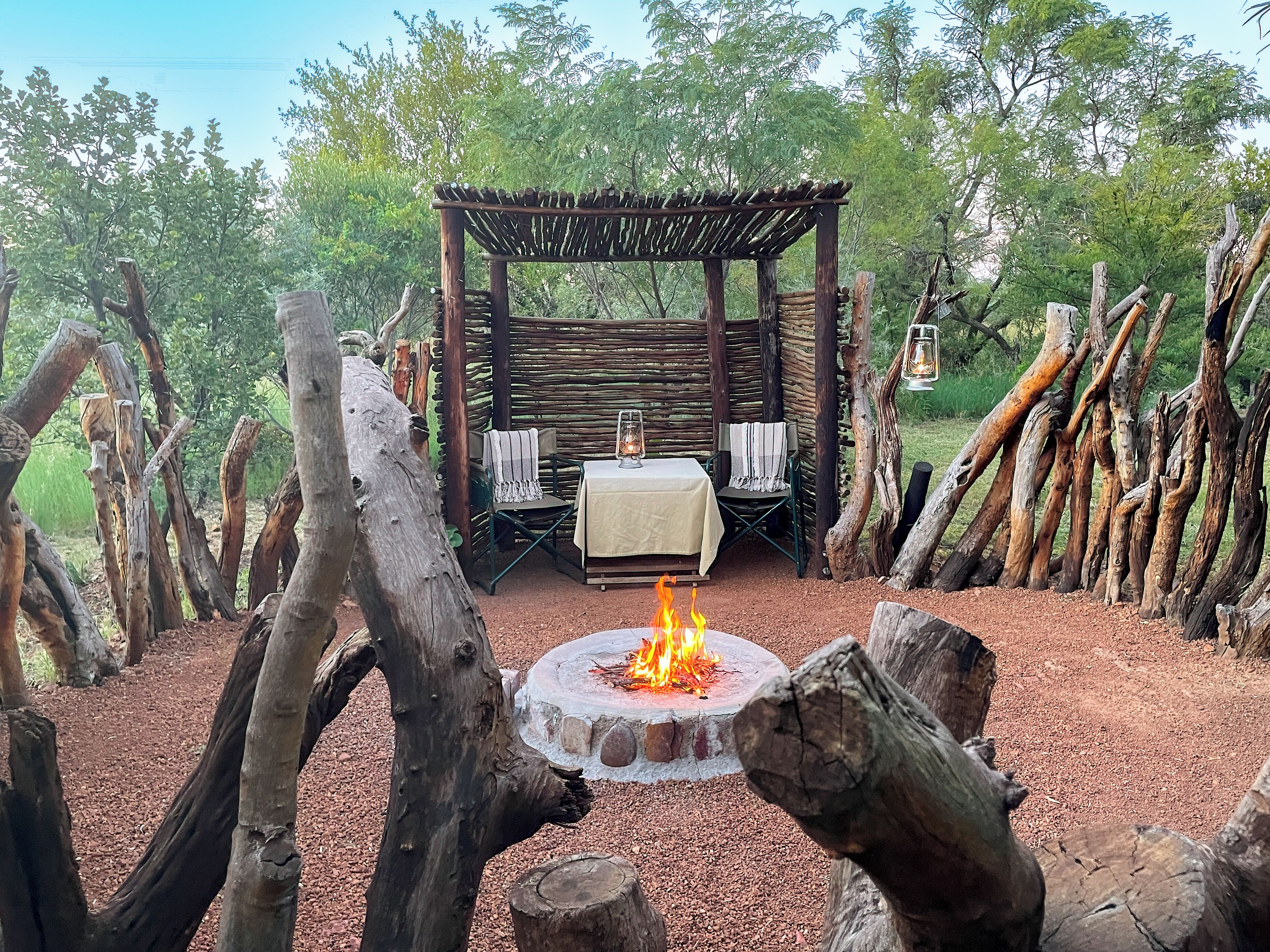 Ein Sitzbereich im Freien mit Feuerschale, einer Holzpergola und Stühlen.