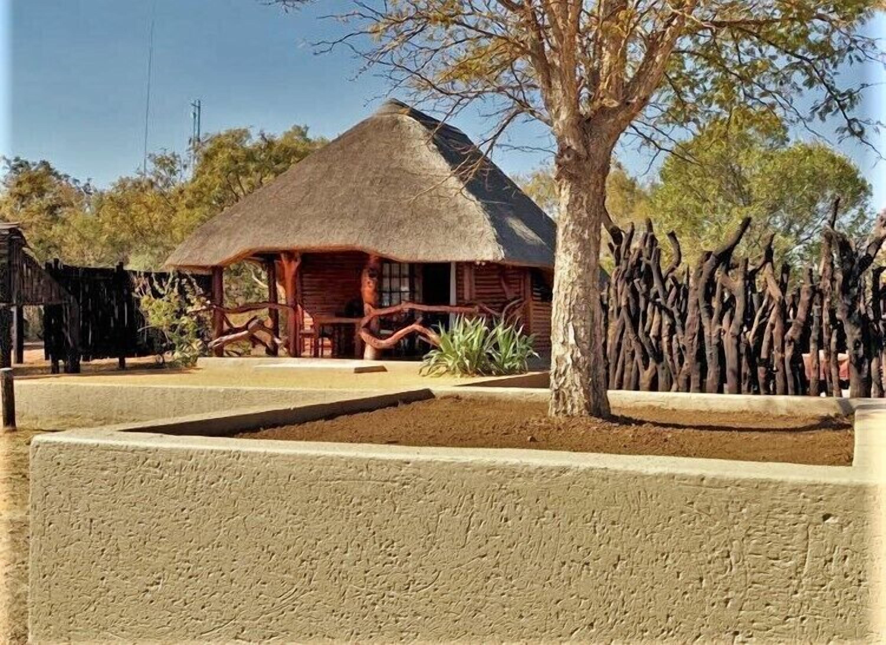 A thatched-roof building with a wooden porch, surrounded by a low concrete wall and a wooden fence.