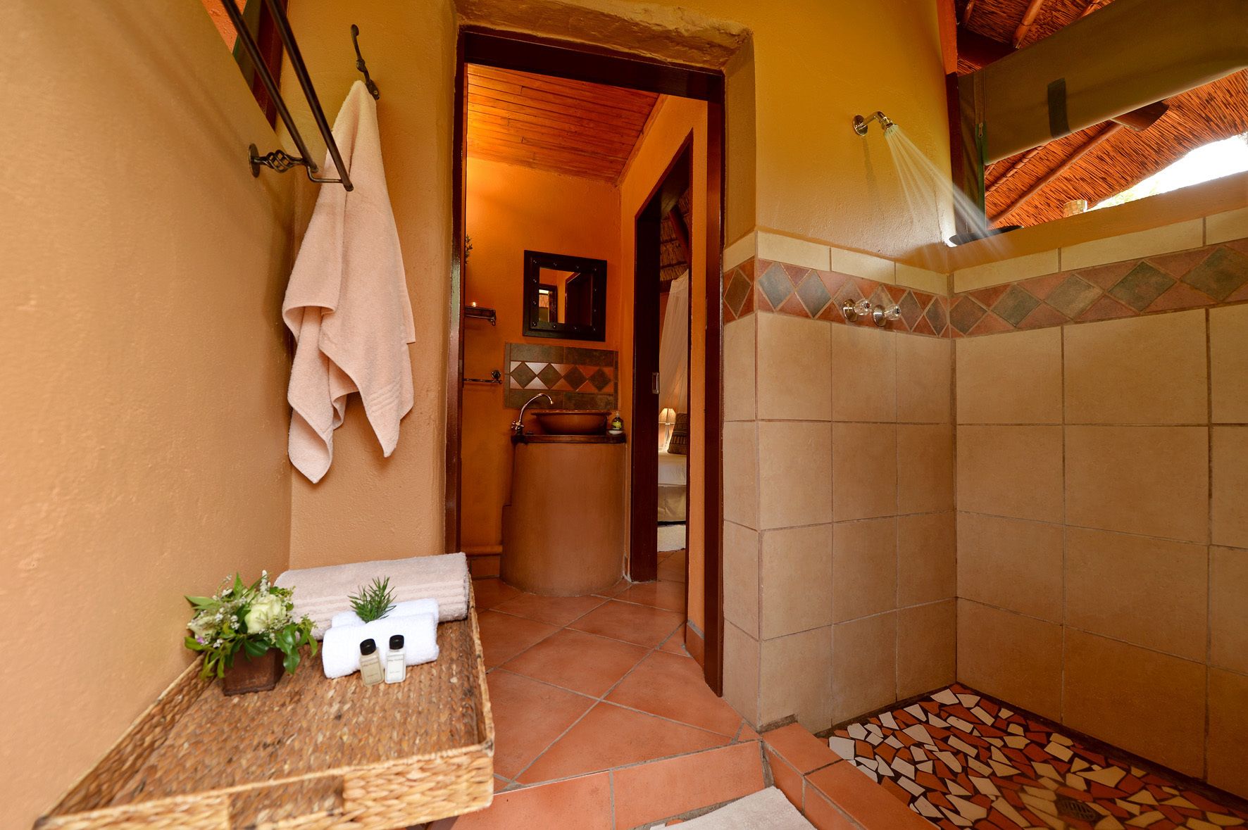 A bathroom with a tiled shower, a wooden bench with toiletries, and a hanging towel.