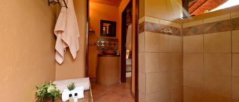 A bathroom with a tiled shower, a wooden bench with toiletries, and a hanging towel.