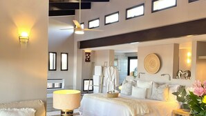 Ein geräumiges Schlafzimmer mit einem großen Bett, Nachttischen, einem Deckenventilator und Blick zur Küche.