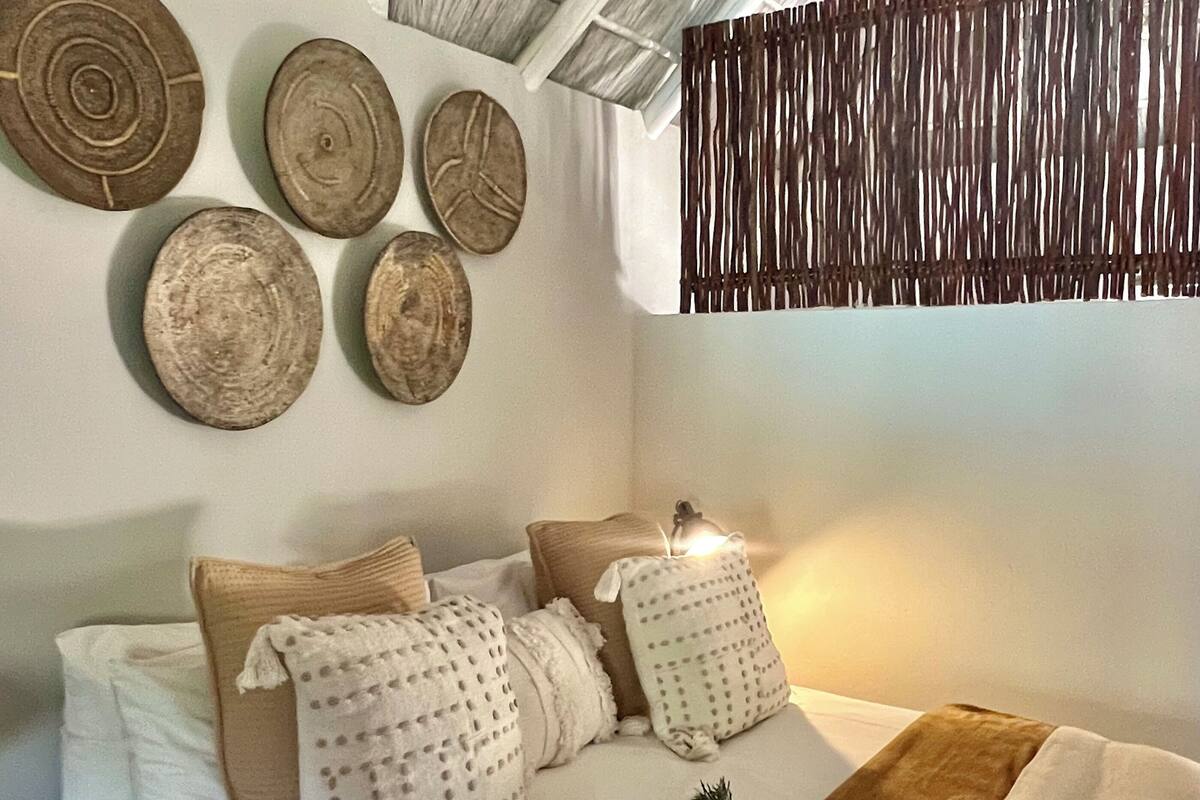 Une chambre avec un plafond haut, un lit recouvert de plusieurs coussins, une tapisserie murale tissée et un ventilateur de plafond.