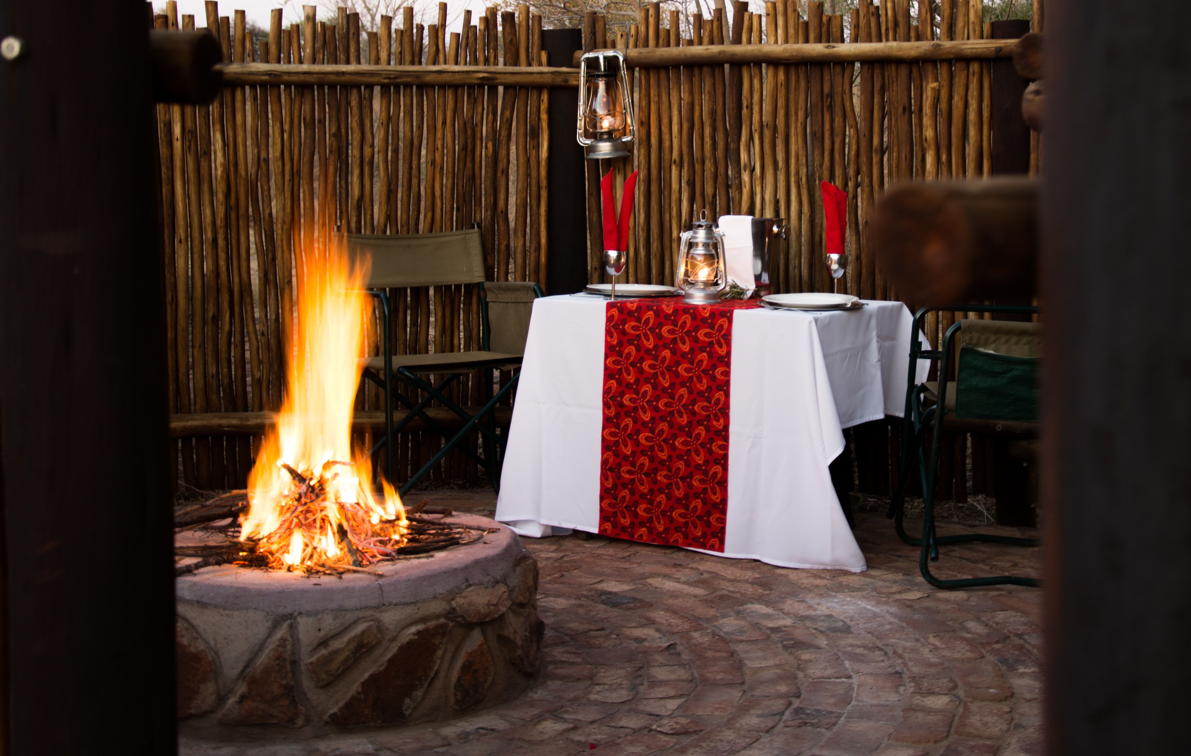 An outdoor dining area with a stone fire pit and a table set with a white tablecloth and red accents.