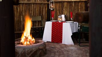 An outdoor dining area with a stone fire pit and a table set with a white tablecloth and red accents.
