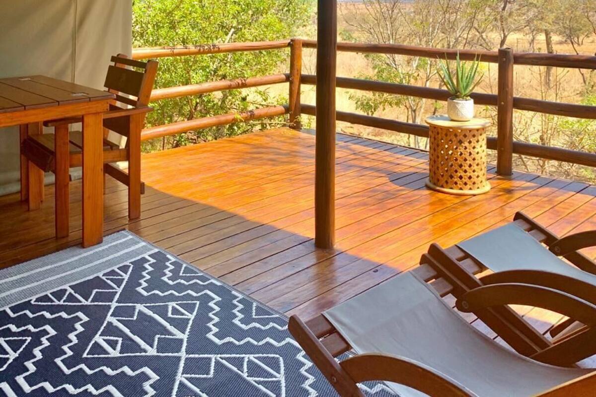 Une terrasse en bois avec une table et des chaises, un tapis à motifs et une plante en pot.