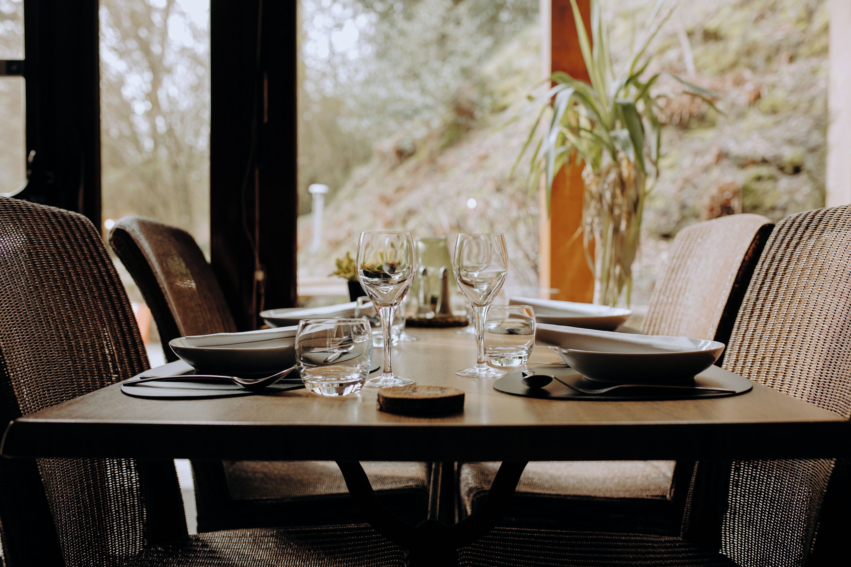 Une table à manger dressée avec des assiettes, des couverts et des verres à vin, entourée de chaises.