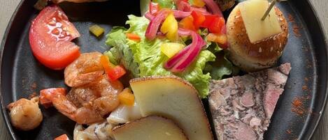 Un plato de comida con diferentes elementos, incluyendo algo a la parrilla, un trozo de carne, verduras y una loncha de queso.