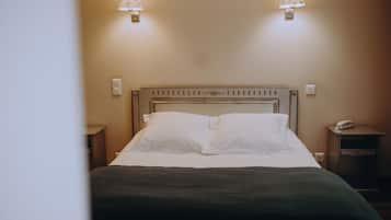 Uma cama bem arrumada com lençóis brancos, duas luminárias fixadas na parede e um telefone ao lado da cama.