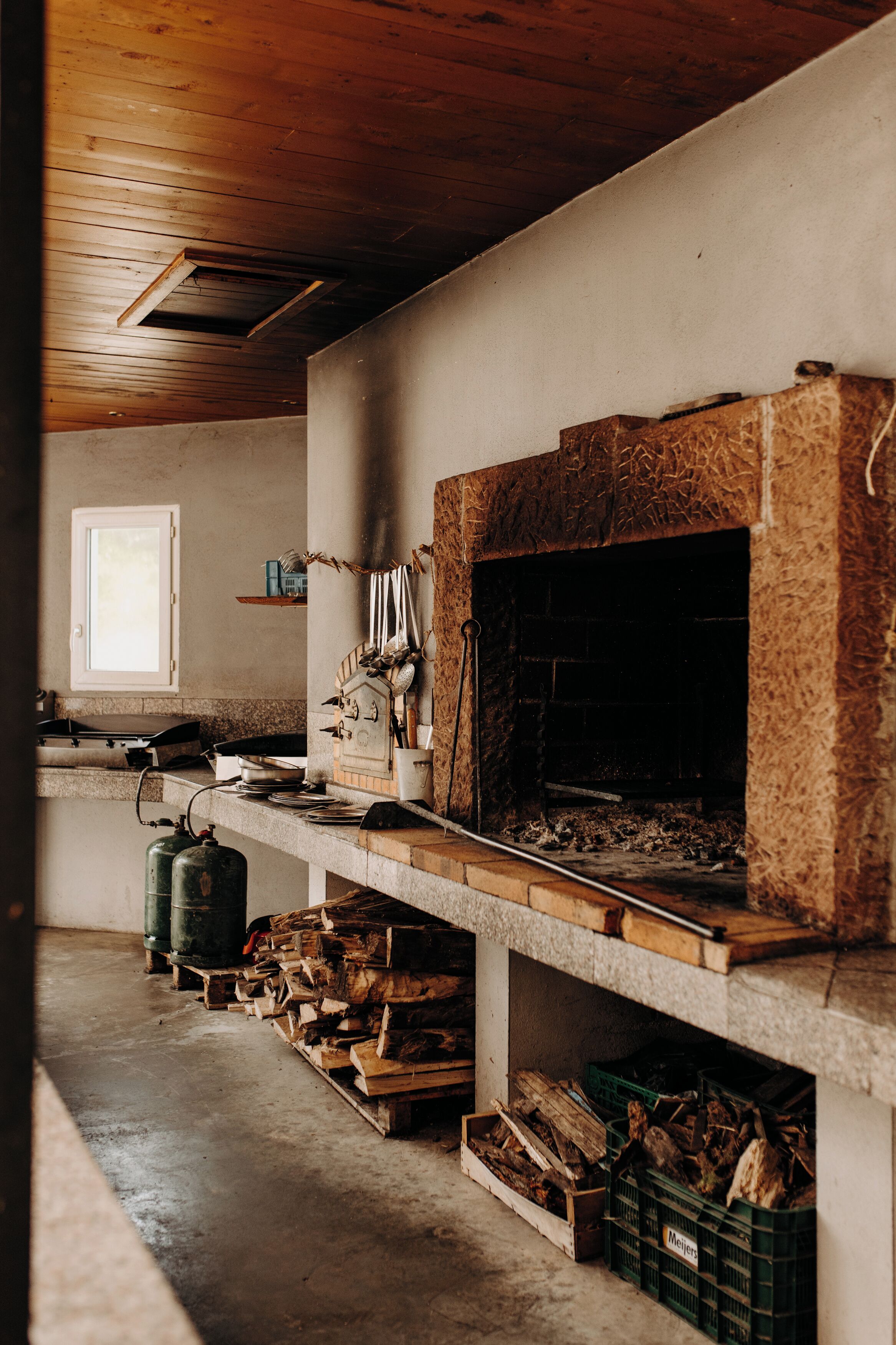 Una cocina rústica con estufa de leña, una ventana y suelo de concreto.