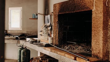 Una cocina rústica con estufa de leña, una ventana y suelo de concreto.