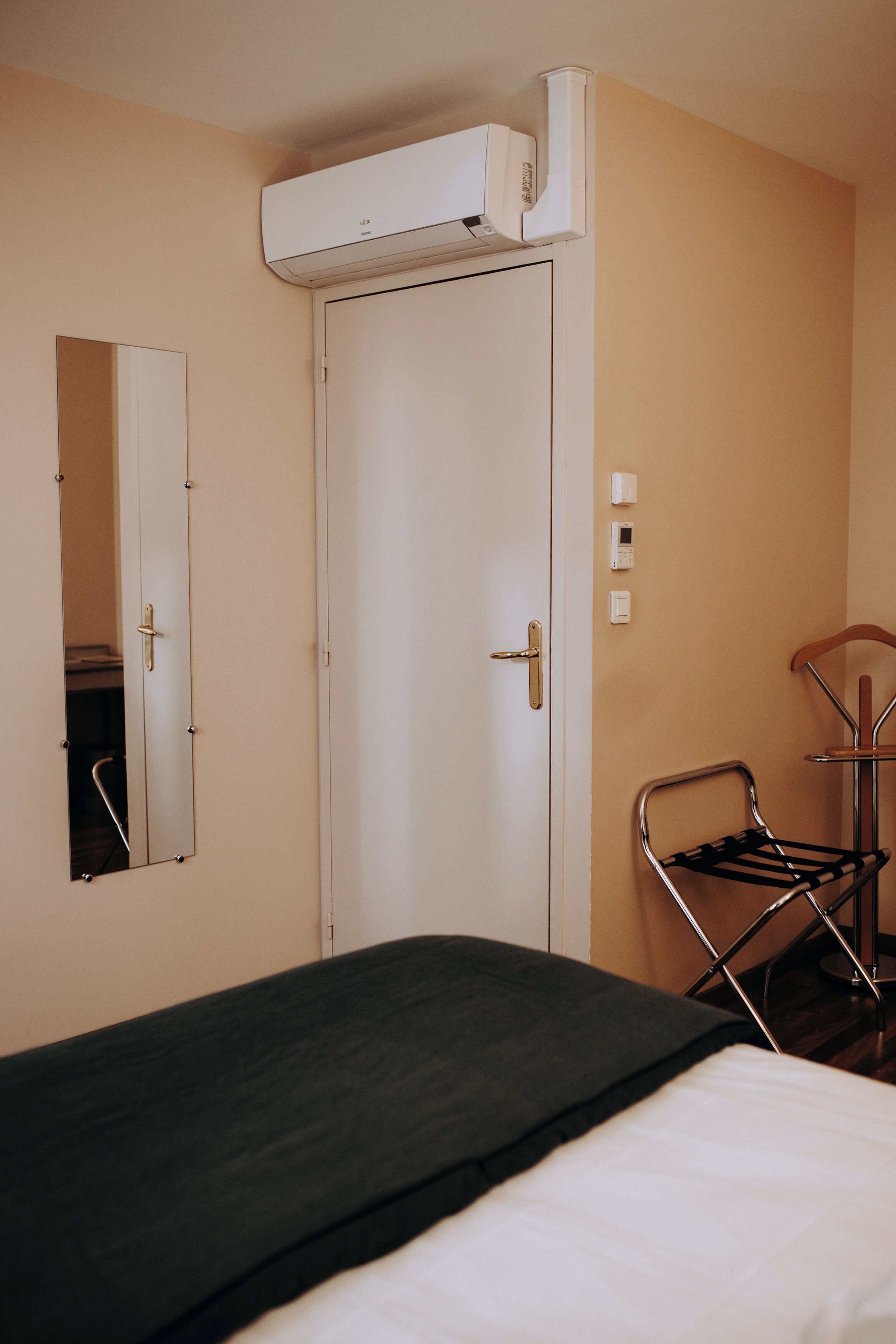 Quarto de hotel com cama, espelho, porta e ar condicionado.