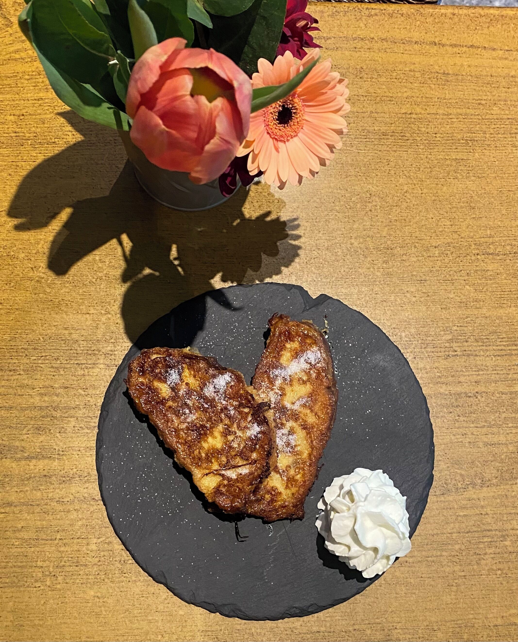 Un plato con dos porciones de comida frita y una cucharada de crema sobre una losa oscura.