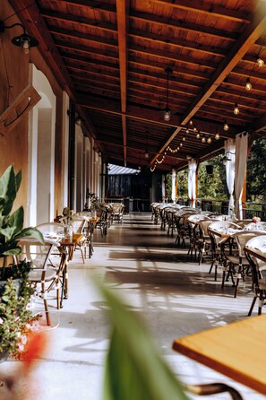 A covered outdoor dining area with tables and chairs, wooden beams, and hanging light fixtures. - Logis Hôtel du Parc (Cransac)