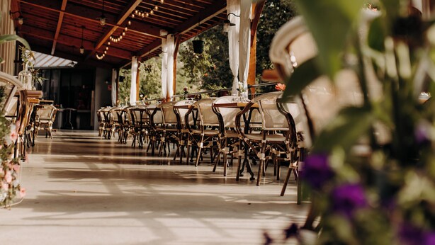 An outdoor covered patio with wooden beams, tables, chairs, and hanging lights. - Logis Hôtel du Parc (Cransac)