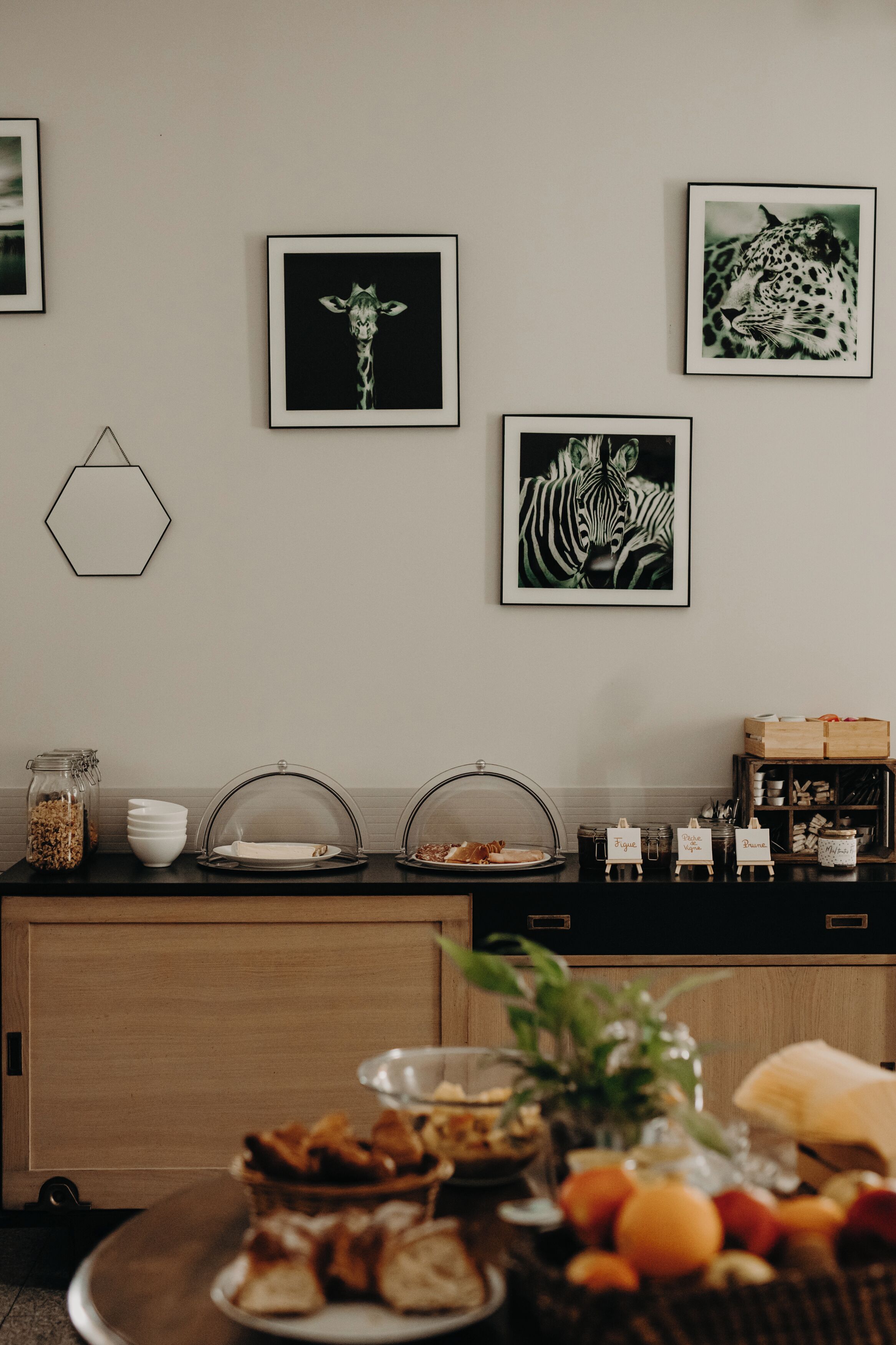 Un buffet de petit-déjeuner proposant une variété d’aliments, une décoration murale hexagonale et des reproductions d’œuvres d’art représentant des animaux, encadrées.