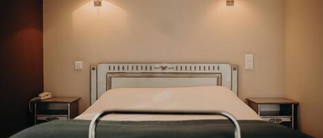 A hotel room with a bed, two bedside tables, and wall-mounted lamps.