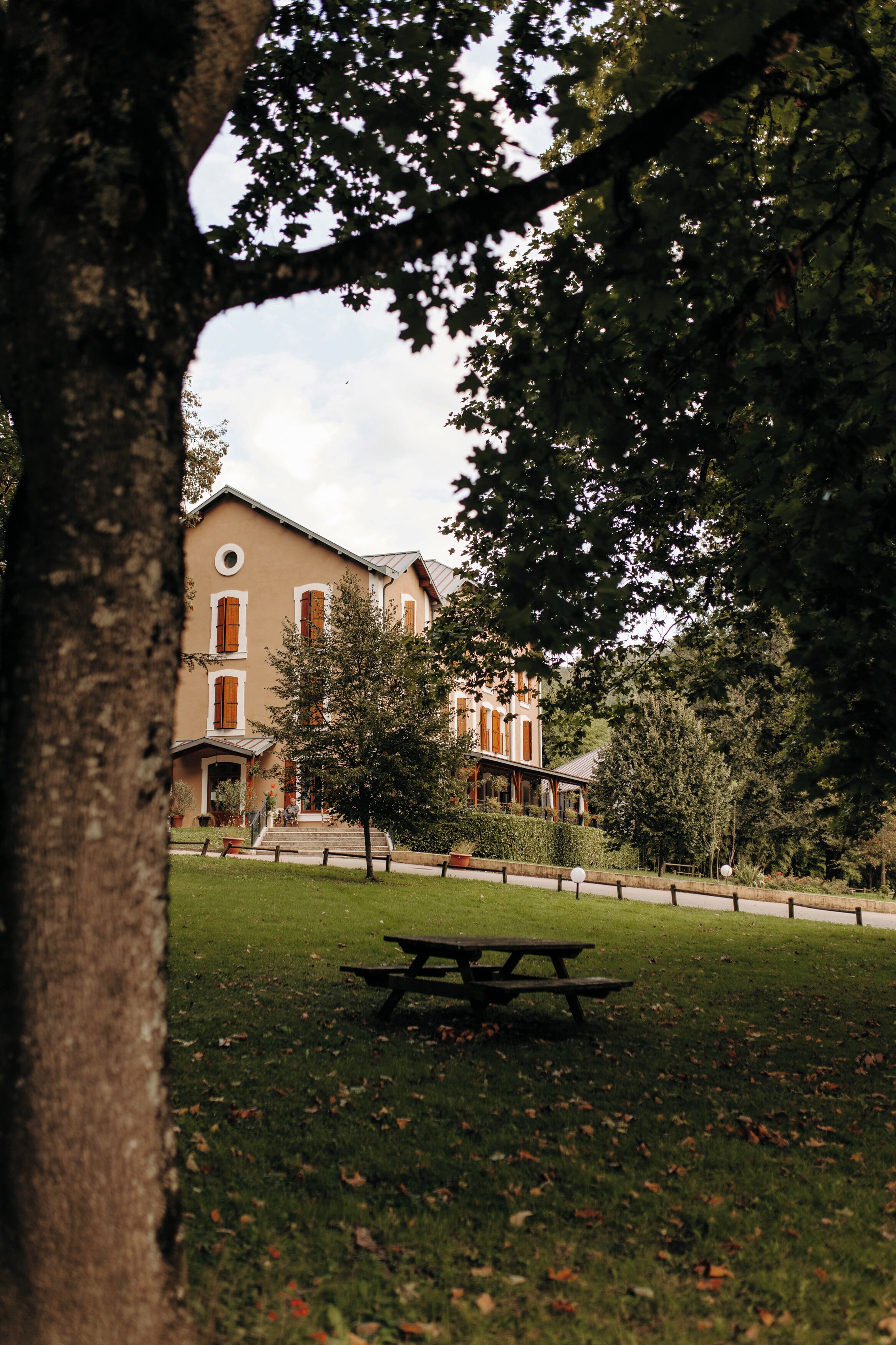 A building with a large lawn, a picnic table, and a tree in the foreground.