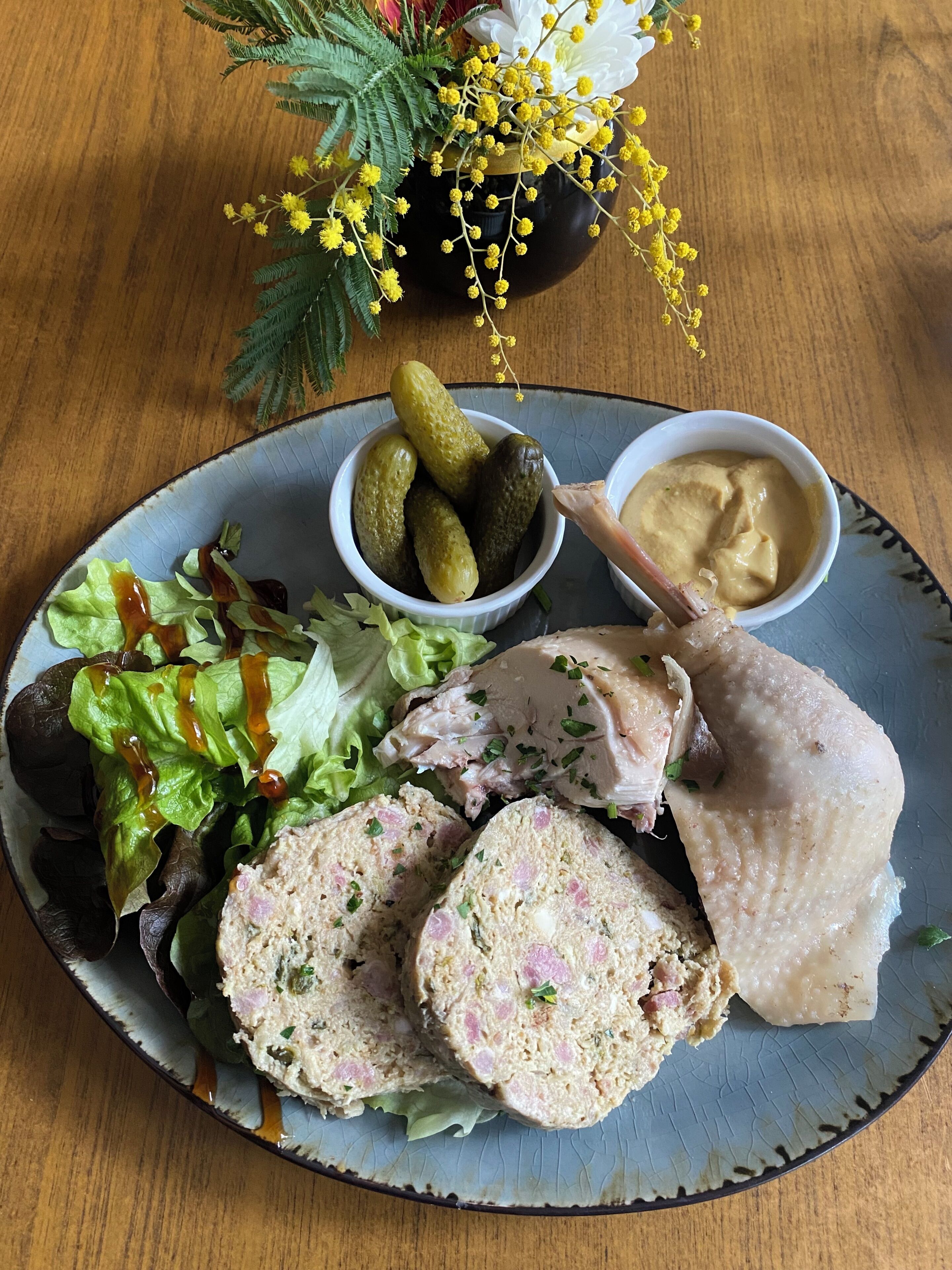 A plate with sliced meatloaf, pickles, and a salad on a ceramic plate.