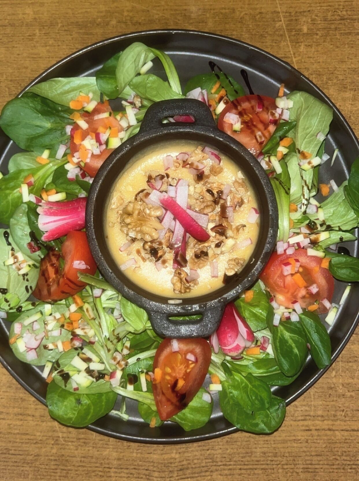 Una sartén negra llena de una sopa cremosa, rodeada de una ensalada con diversas verduras.
