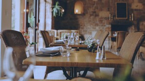 A restaurant with wooden tables, wicker chairs, and a stone wall in the background. - Logis Hôtel du Parc (Cransac)
