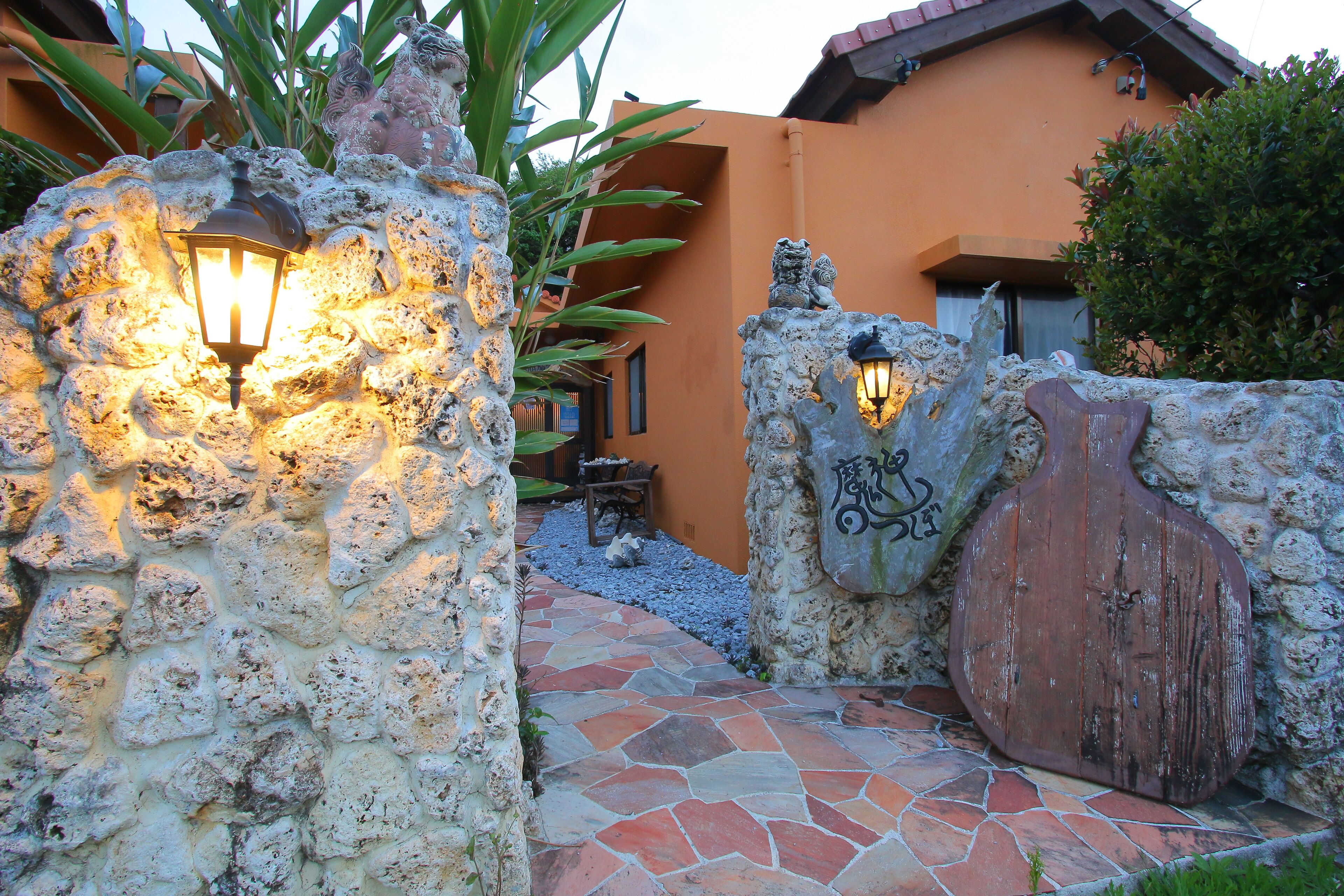 A stone pathway leading to a rustic building with a wooden door and decorative wall lights.
