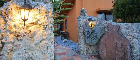 A stone pathway leading to a rustic building with a wooden door and decorative wall lights.