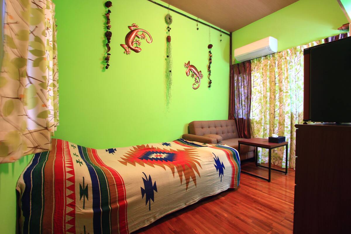 Une pièce avec un mur vert, un canapé, un fauteuil, une petite table et un téléviseur.