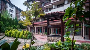 A courtyard with a stone pathway, potted plants, and a covered seating area. - Orbilux (Bansko)