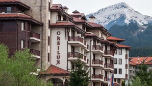 A multi-story hotel with balconies and a mountain backdrop. - Orbilux (Bansko)