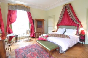 Ein Schlafzimmer mit einem großen Bett, einer Bank, einem Holzkasten, einem Stuhl und einem Schreibtisch.