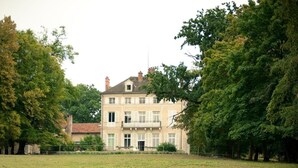 A large, two-story building with a symmetrical facade, surrounded by lush greenery and trees. - Le Château de la Vierge (Bures-sur-Yvette)