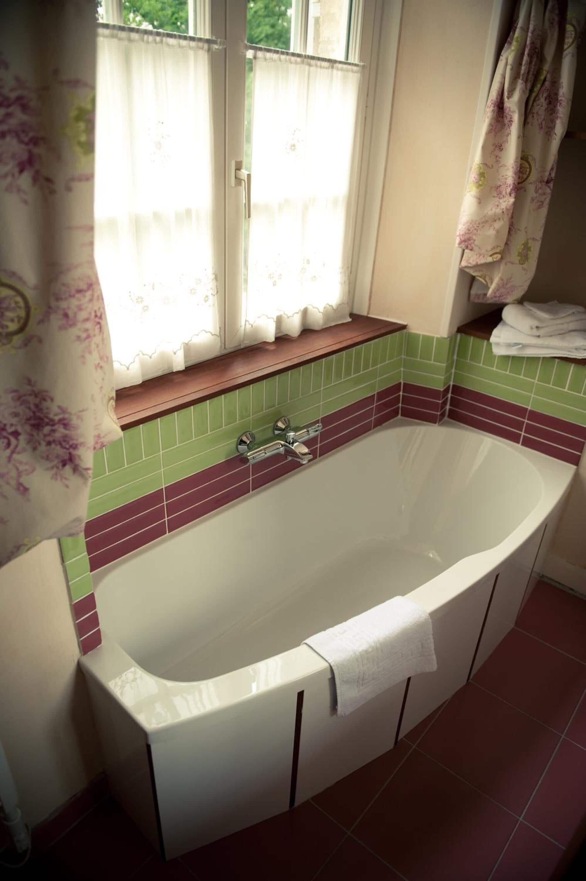 A bathroom with a freestanding bathtub, a window with curtains, and a tiled backsplash.