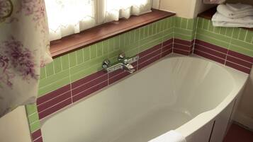 A bathroom with a freestanding bathtub, a window with curtains, and a tiled backsplash.