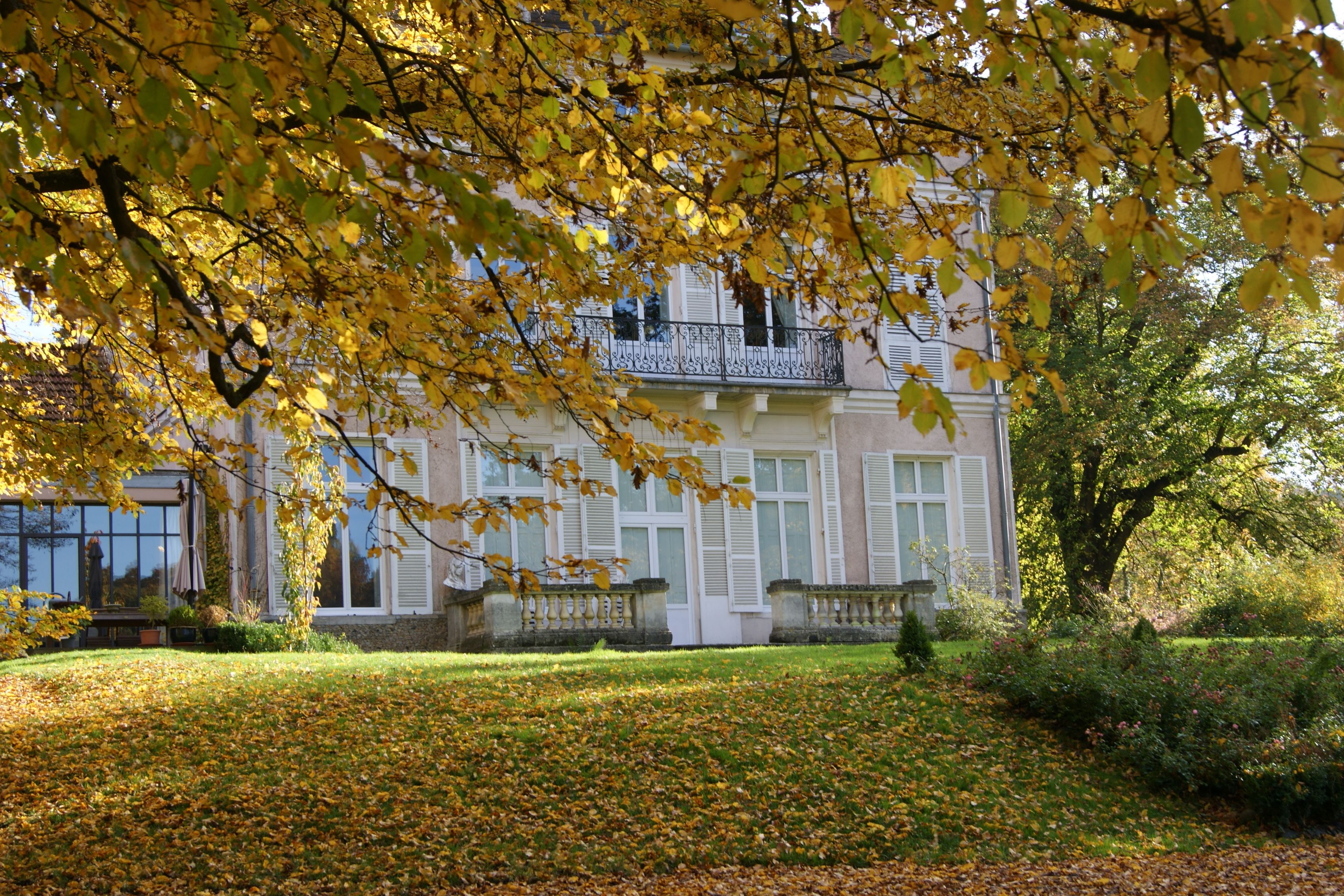 A building with a balcony, surrounded by a garden with fallen leaves.
