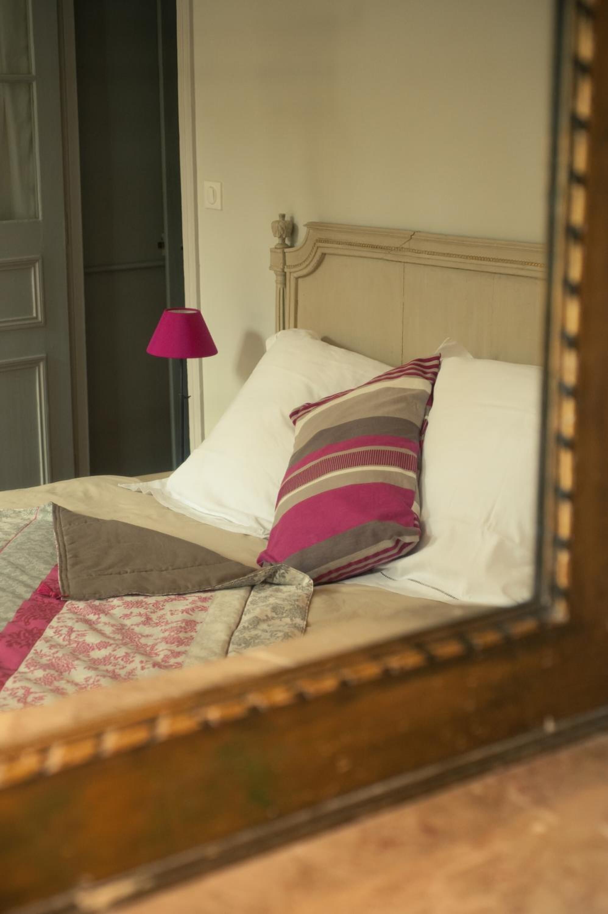 A bed with a wooden headboard, a pink lamp, and a striped pillow.