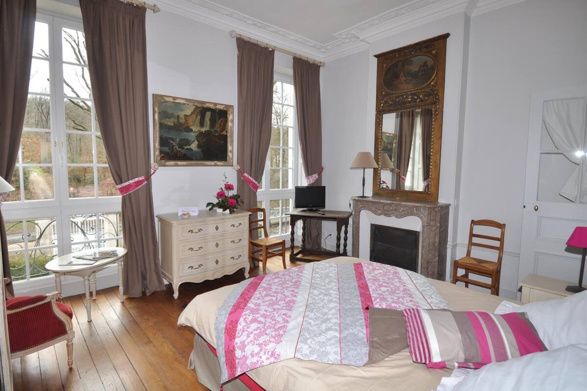 Ein Schlafzimmer mit einem großen Bett, einem Schminktisch, einem Sessel, einem Tisch, einem Kamin und einem Bild an der Wand.