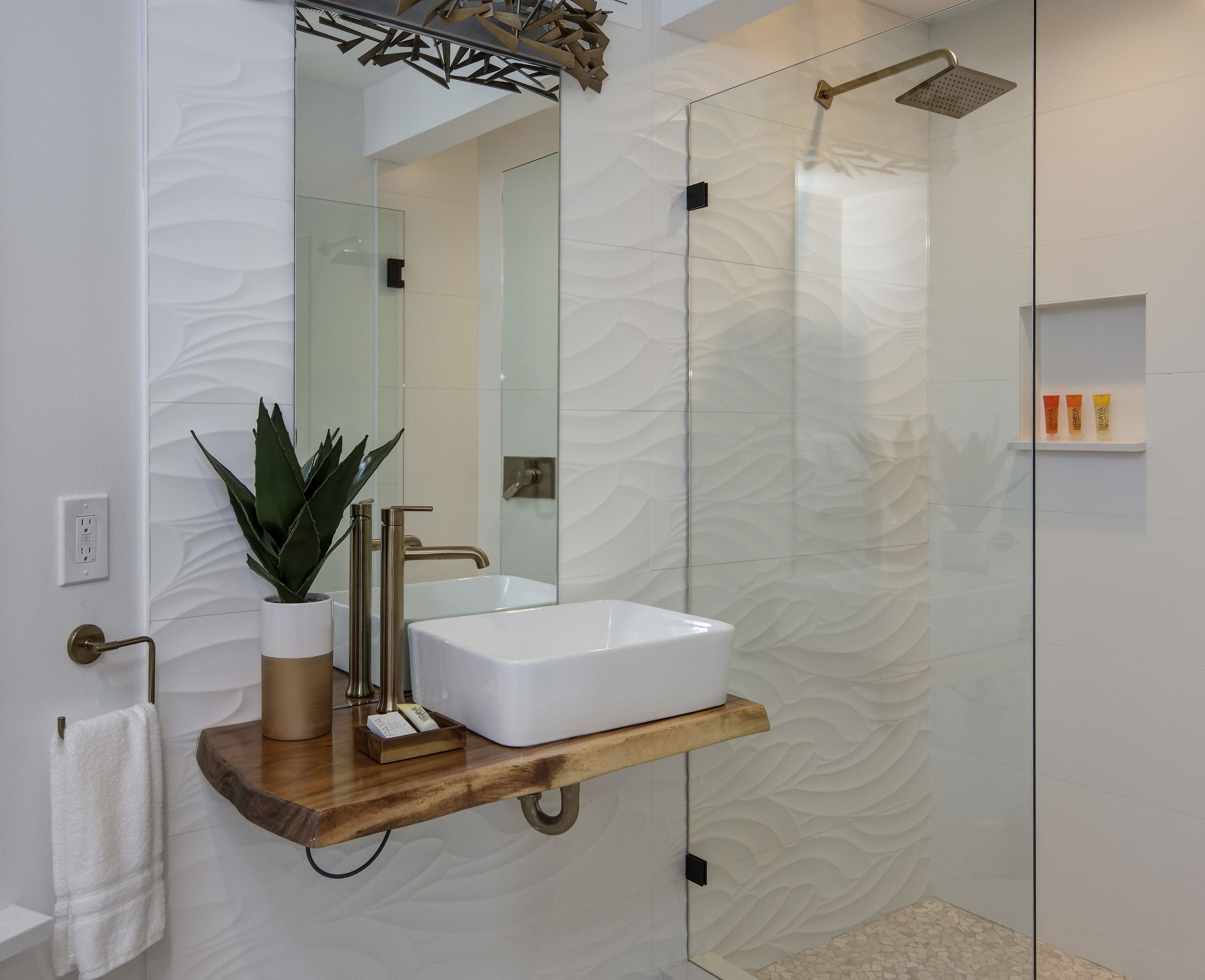 Un baño moderno con cabina de ducha de vidrio, un lavabo blanco y un estante de madera.
