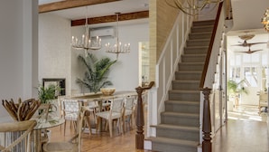 A spacious living area with a wooden staircase, a dining table with chairs, and a large plant. - Casablanca (Cape May)