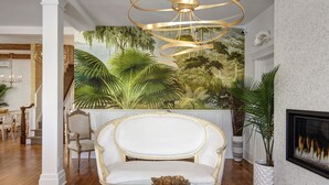 A living room with a white sofa, a glass coffee table, and a mural of tropical foliage on the wall. - Casablanca (Cape May)
