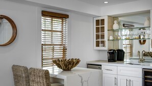 A modern kitchen with white cabinetry, a marble countertop, wicker chairs, and a glass display cabinet. - Casablanca (Cape May)