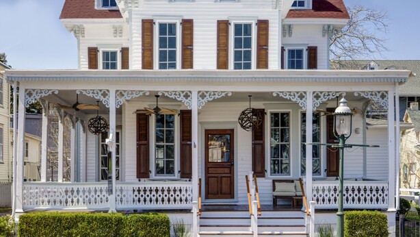 A two-story white house with a porch, wooden shutters, and a red roof. - Casablanca (Cape May)
