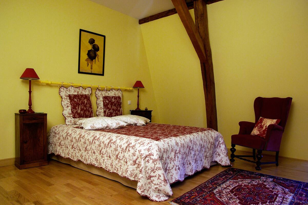 A bedroom with a bed, two bedside lamps, a chair, a rug, and a painting on the wall.