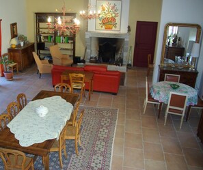A cozy living room with a fireplace, a dining area with a table and chairs, a bookshelf, and a red sofa. - La Bastide du Roy (Villamblard)