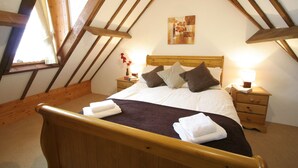 A bedroom with a wooden ceiling, a bed with white linens, a nightstand with a lamp, and a painting on the wall.