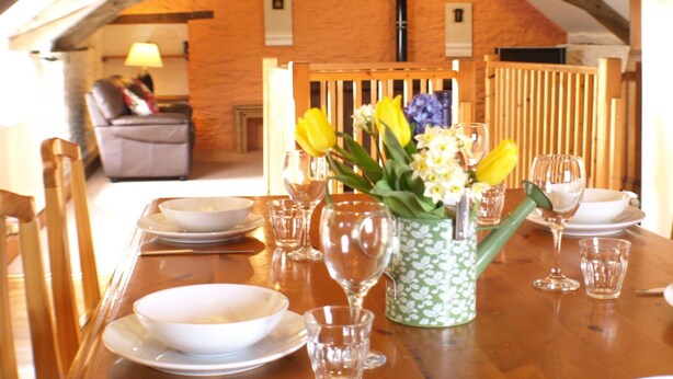 Una mesa de comedor preparada con platos, tazones y vasos, con un florero de flores en el centro.