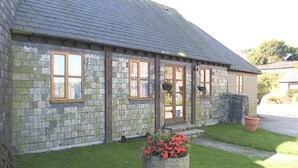 A stone building with a sloped roof, multiple windows, and a small garden area with flowers.